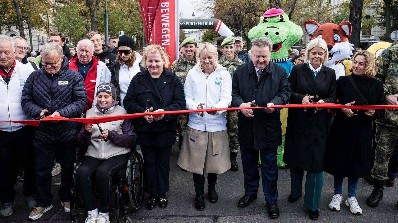 © ORF/Thomas Jantzen Mehrere Menschen stehen hinter einem roten Band, sie halten Scheren in der Hand. Es sind Sport Austria-Präsident Hans Niessl, Rollstuhltennis-Profi Lena Lichtenegger, Bundesministerin Corinna Schumann, Staatssekretärin Michaela Schmidt, Bürgermeister Michael Ludwig, Bundesministerin Klaudia Tanner und Lisa Zuckerstätter (ORF). Hinter ihnen sind Soldat*innen, Vereins-Maskottchen und eine wartende Menschenmenge zu sehen.