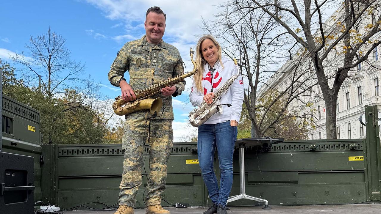 © ORF/Alexandra Fida Ein Bundesheer-Soldat in Uniform und Saxophonistin Angela Walter im WBÖ-Hoodie auf einem als Bühne umfunktionierten LKW mit ihren Saxophonen.