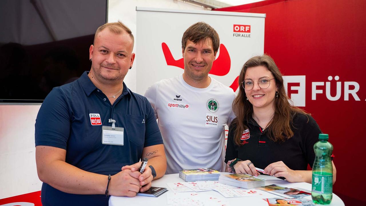 © ORF/Osman Cetin In einem ORF Eventzelt stehen drei Personen dicht beisammen hinter einem weißen Stehtisch mit Infomaterial. Eine Person trägt ein "Sporthilfe"-Shirt, die anderen beiden dunkelblaue Polos mit dem Logo des österreichischen Zolls.
