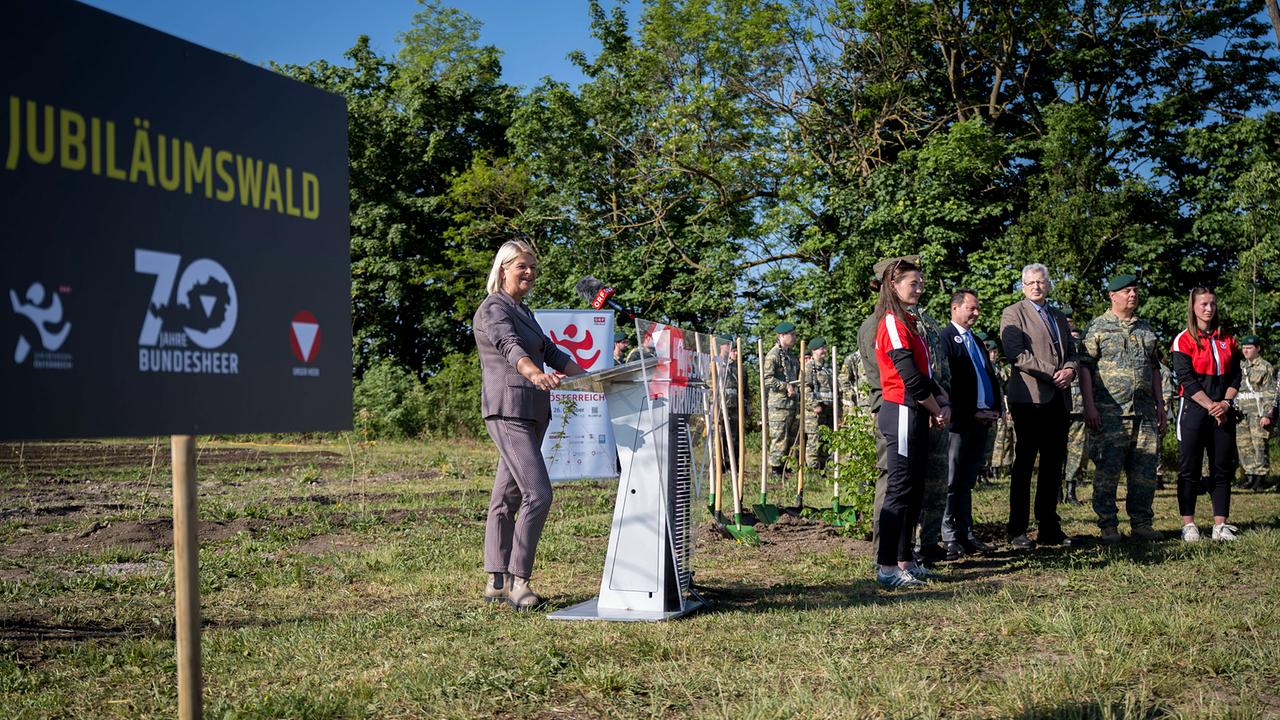 Verteidiungsministerin Klaudia Tanner am Podest, im Hintergrund stehen Soldat*innen mit Spaten bereit
